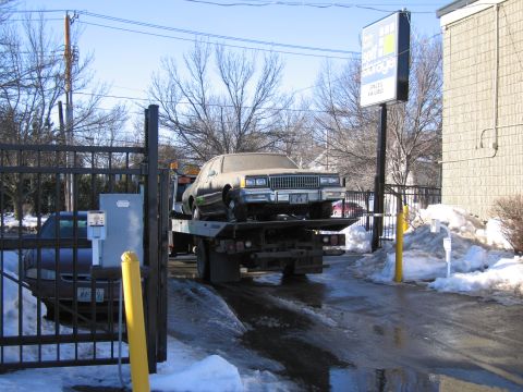 1991 Ford LTD Crown Victoria - Photograph of a sedan on a tow truck entering a storage gate, not a technical document.