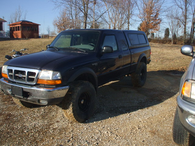 Black Ford Ranger pickup truck with camper shell and lifted suspension parked on gravel.