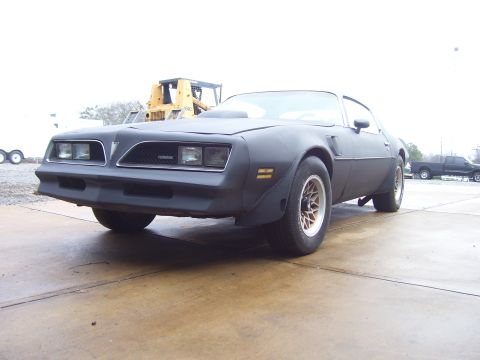 1978 Pontiac Trans Am - A matte black 1977 Pontiac Firebird is parked outdoors with a construction vehicle in the background.