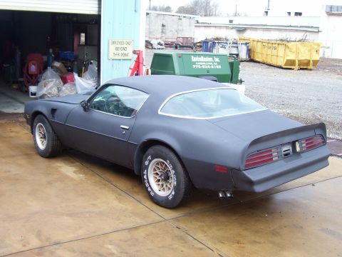 1978 Pontiac Trans Am - This matte gray coupe, likely a 1977 model, is parked outside a garage with industrial dumpsters in the background.