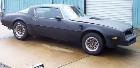 1978 Pontiac Trans Am - A matte black Pontiac Firebird is parked outside a garage with its hood slightly ajar.