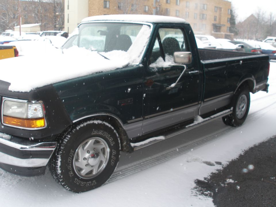 Dark green pickup truck with snow on hood and roof, side view