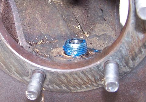 1990 Ford Bronco - A greased threaded plug is surrounded by rusty metal and wheel studs, indicating a mechanical part.