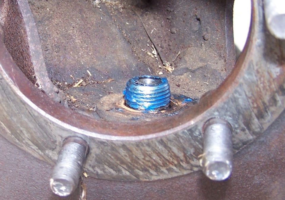 Close-up of a greased threaded plug and two wheel studs on a rusty metal component