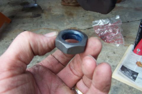 1990 Ford Bronco - A hex nut with blue threadlocker is held in a hand, with a plastic bag and papers in the background.