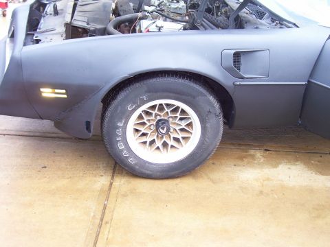 1978 Pontiac Trans Am - The front quarter panel and wheel of a 1978 Pontiac Trans Am are visible, with the hood open to reveal the engine bay.