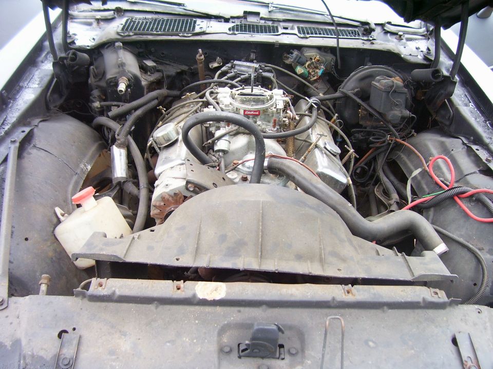Engine bay with V8 engine and carburetor. SuperMotors.net logo visible