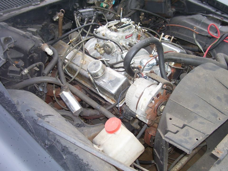 Engine bay view showing V8 engine, carburetor, alternator, and hoses