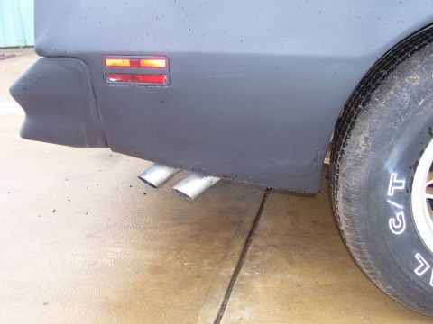 1978 Pontiac Trans Am - Close-up of the rear bumper and dual exhaust pipes on a 1978 Pontiac Trans Am, with a tire visible on the right.