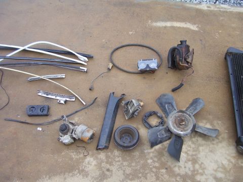 1978 Pontiac Trans Am - A collection of disassembled car parts, including trim pieces, a fan, and radiator, are laid out on a concrete surface.