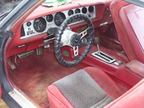 1978 Pontiac Trans Am - The interior of a car shows red upholstery and a dashboard with gauges and a steering wheel.