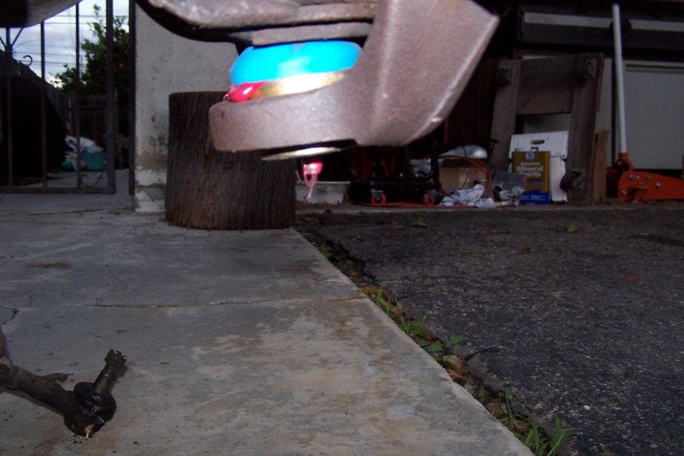 Close-up of a ball joint with blue boot and pink grease, part of a vehicle's suspension system