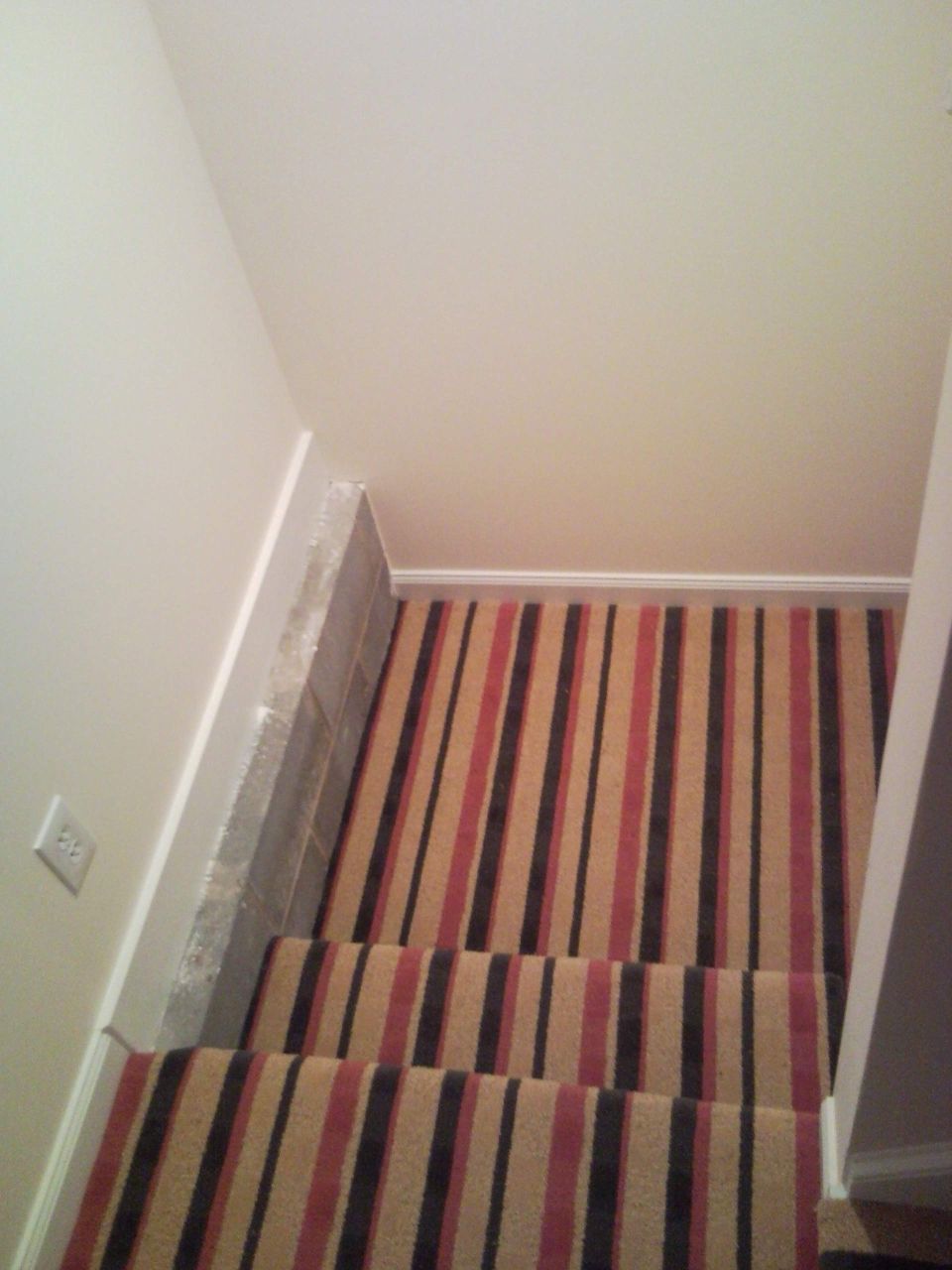 Carpeted staircase with tan, red and black striped carpet inside a house