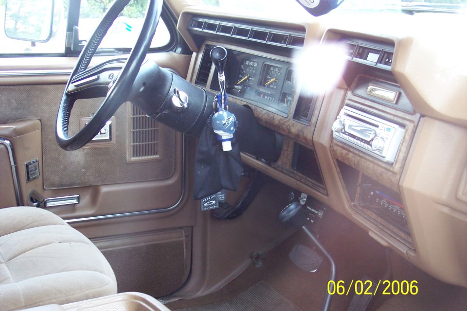 Tan 1986 Ford Bronco interior with black steering wheel, woodgrain dash trim, and aftermarket CD stereo