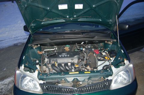 2001 Toyota Echo - The engine bay of a green 2001 Toyota Echo is visible with the hood raised.