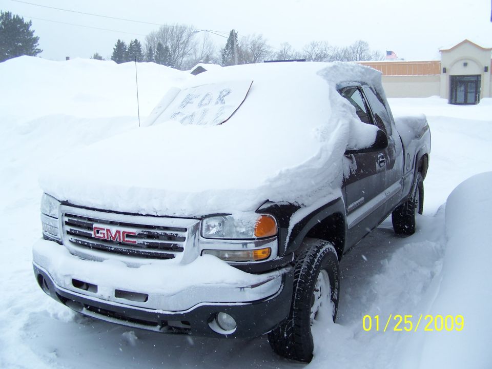 GMC truck buried in snow, 'For Sale' sign on windshield