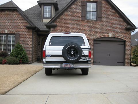 1996 Ford Bronco - Rear view of a white 1996 Ford Bronco with black racing stripes and a spare tire on the back.