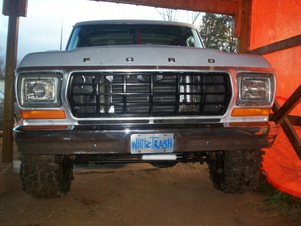 Silver Ford truck front view, chrome bumper, black grille, 'White Trash' license plate, large tires