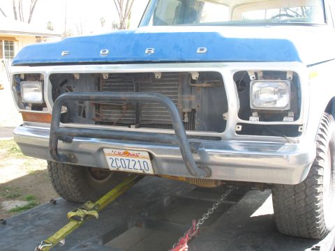 1987 Ford Bronco - Front view of a Ford truck with a blue hood and a chrome bumper, showing a missing grille section.