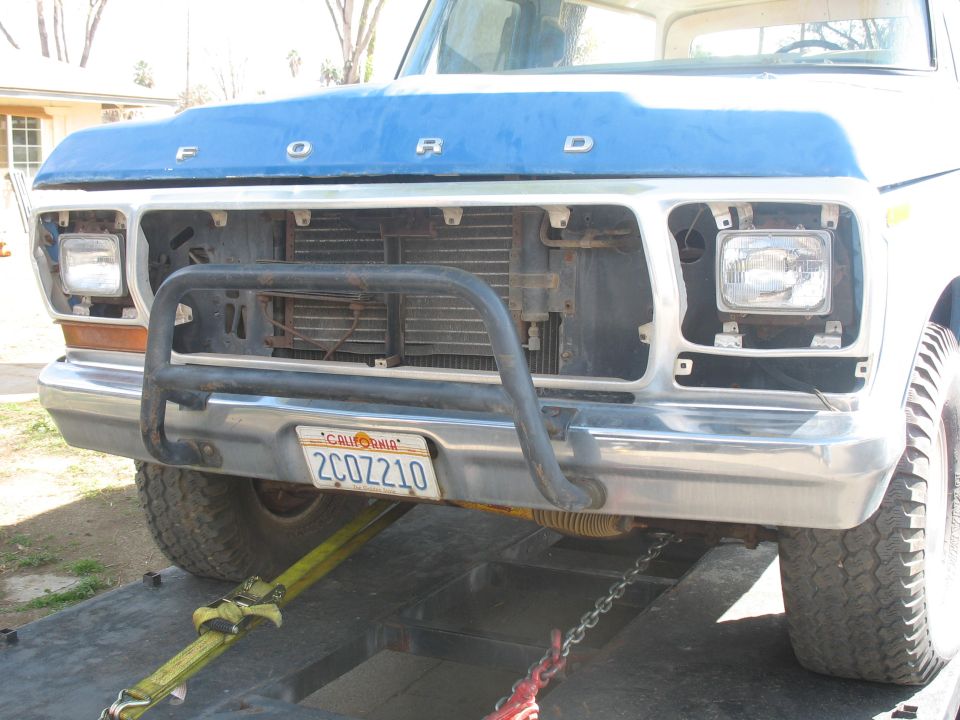 Ford truck front end with blue hood, chrome bumper, and grille missing headlights