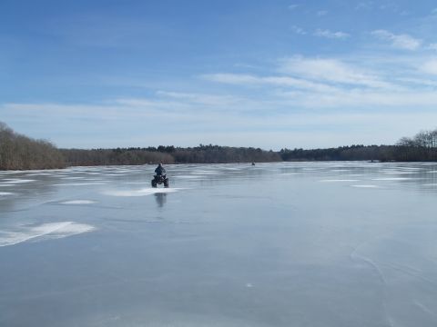 1995 Ford Mustang - An ATV rides across a frozen lake under a partly cloudy sky, with trees lining the distant shore.