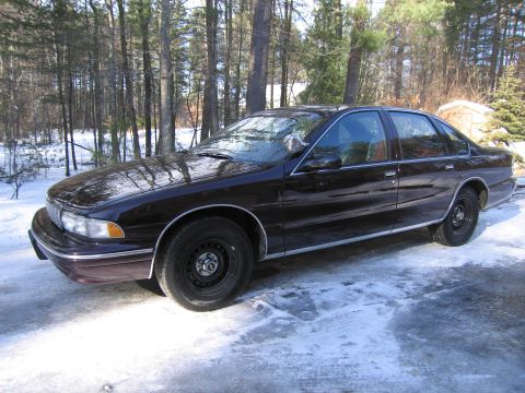 1991 Ford LTD Crown Victoria - A dark-colored sedan sits on a snow-covered surface with trees visible behind it.