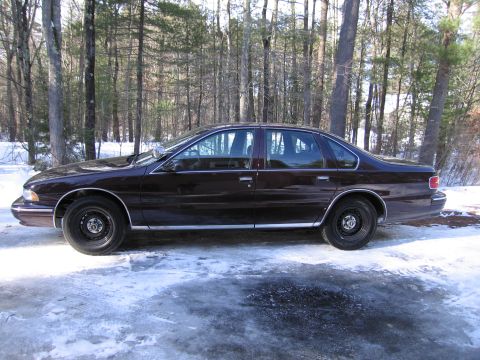 1991 Ford LTD Crown Victoria - A side profile of a dark-colored sedan is captured in a winter setting, surrounded by trees.