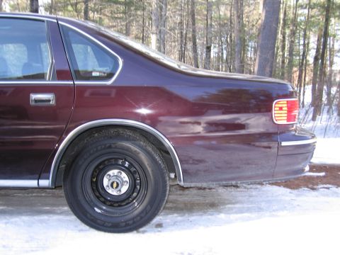 1991 Ford LTD Crown Victoria - Side view of a maroon sedan's rear section, showing the wheel well and taillight assembly.