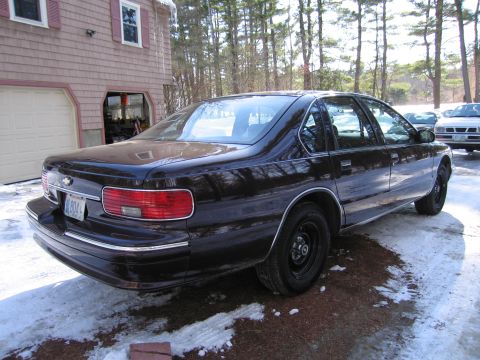 1991 Ford LTD Crown Victoria - A dark maroon/black Chevrolet Caprice full-size sedan photographed from the rear three-quarter angle, showing the Chevy bowtie badge on the…