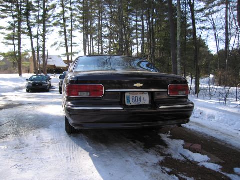 1991 Ford LTD Crown Victoria - Rear view of a black sedan on a snowy road, with another dark vehicle visible in the background.