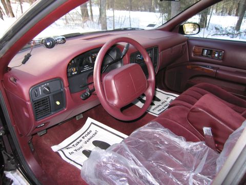 1991 Ford LTD Crown Victoria - The interior of a maroon vehicle features plastic seat covers and floor mats with a 'We Take Pride In Your Vehicle!' message.