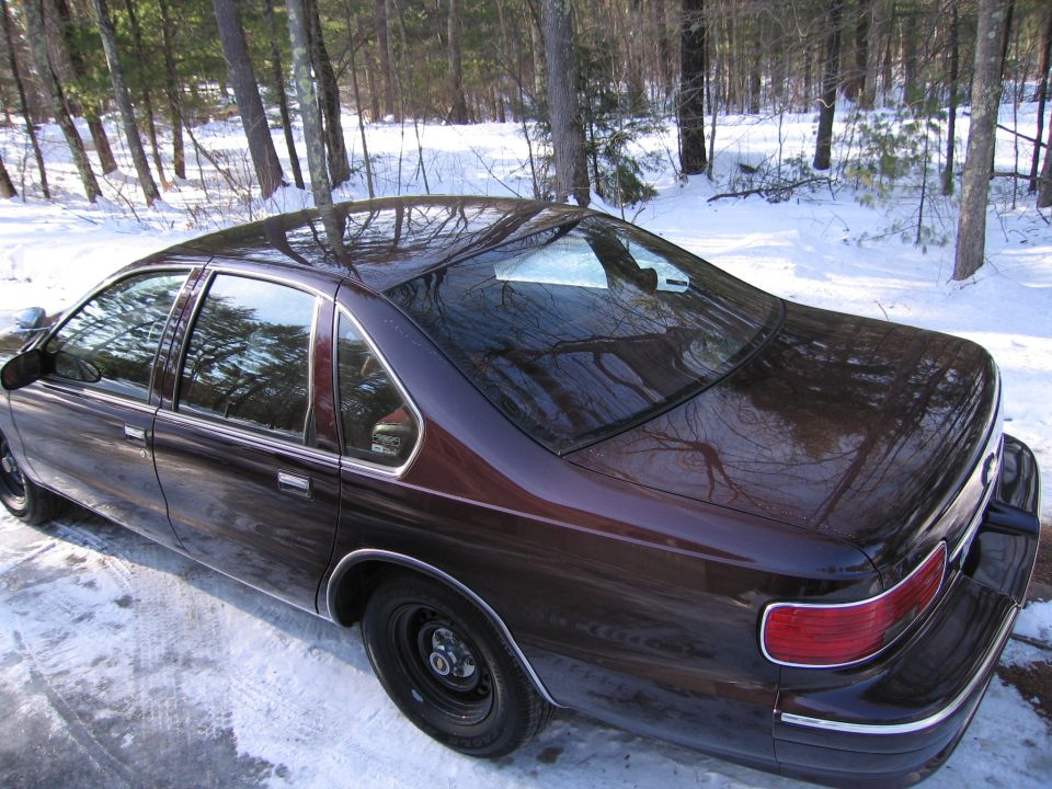 Dark red sedan with black steel wheels parked on a snowy surface, viewed from the rear quarter