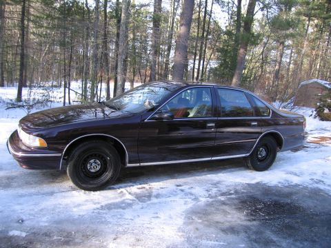 1991 Ford LTD Crown Victoria - A dark-colored sedan is parked on an icy surface surrounded by trees.