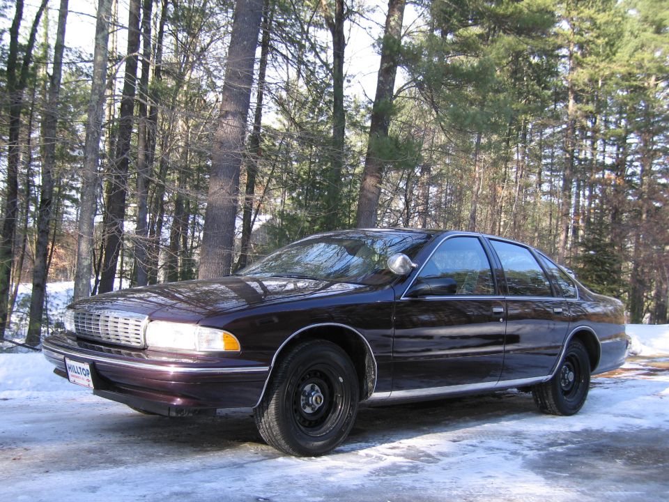 Dark sedan with a chrome grille and a spotlight on the driver's side, parked on a snowy road