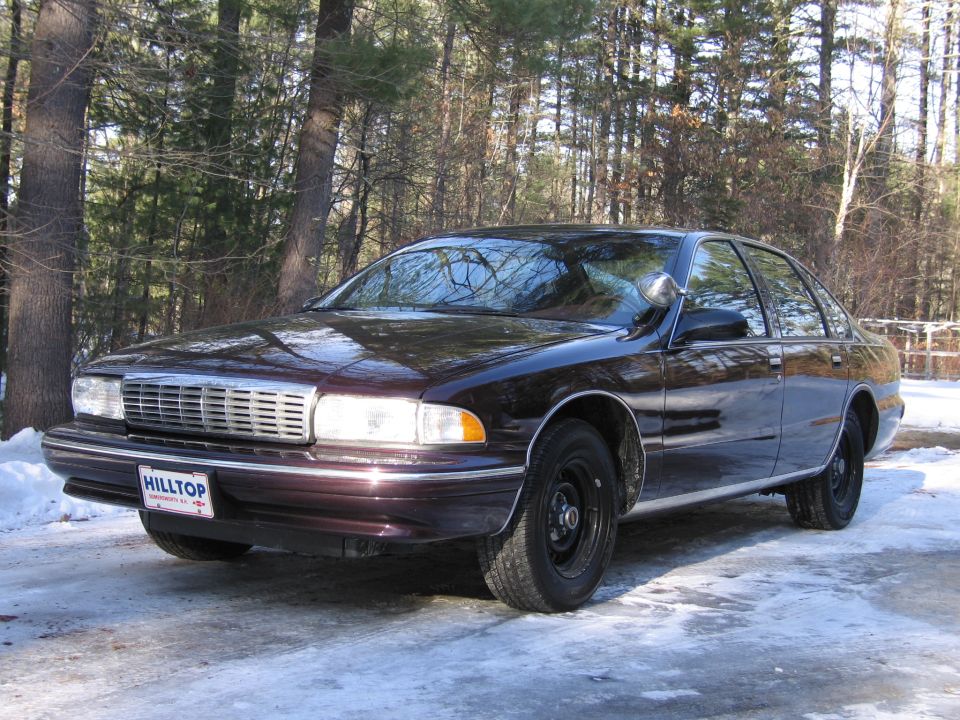 Dark sedan with a chrome grille and a "HILLTOP" license plate, parked on a snowy road