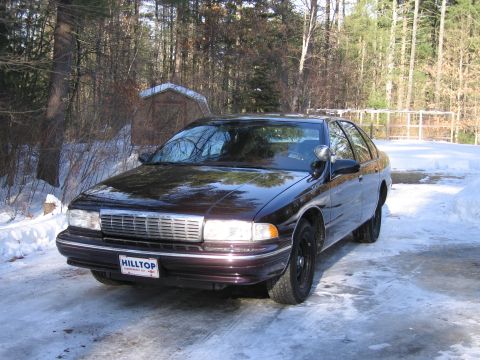 1991 Ford LTD Crown Victoria - This dark sedan, likely a 1994-1996 Chevrolet Caprice, is parked in a snowy area. The grille and body style are characteristic of this era.