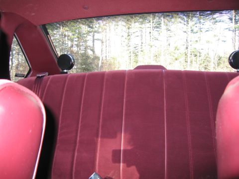1991 Ford LTD Crown Victoria - Interior view of a red velour rear seat with two circular objects mounted on the rear window sill.