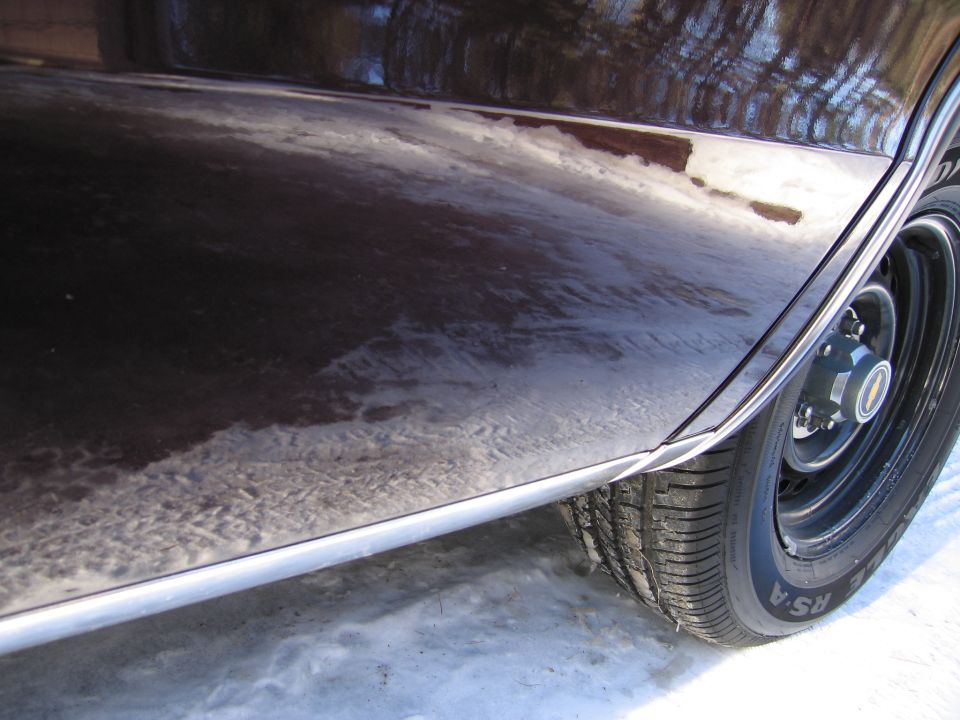 Close-up of a dark-colored car's lower body panel and wheel in snow
