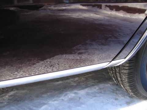 1991 Ford LTD Crown Victoria - The side of a car is shown with reflections on its dark paint, parked in the snow.
