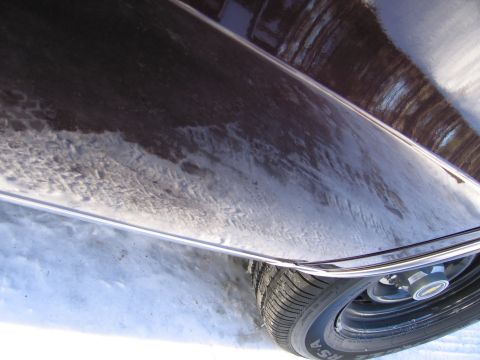 1991 Ford LTD Crown Victoria - Close-up of a dark colored car's lower body panel and tire, partially covered in snow.