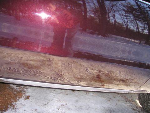 1991 Ford LTD Crown Victoria - A close-up of a maroon car's side panel shows dirt and snow accumulation near the bottom trim.