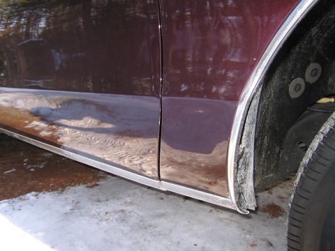 1991 Ford LTD Crown Victoria - Side view of a car's lower door and wheel well, showing chrome trim and tire.