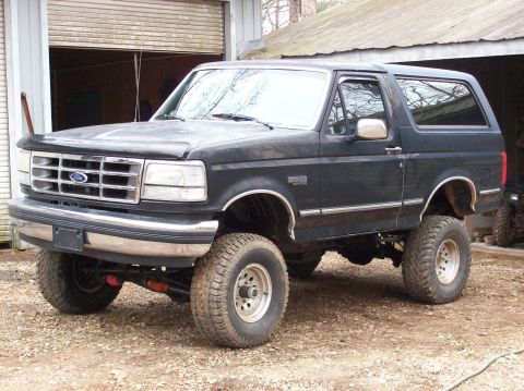 1992 Ford Bronco - This lifted 1992 Ford Bronco is shown from a three-quarter front angle, parked outdoors near a garage.