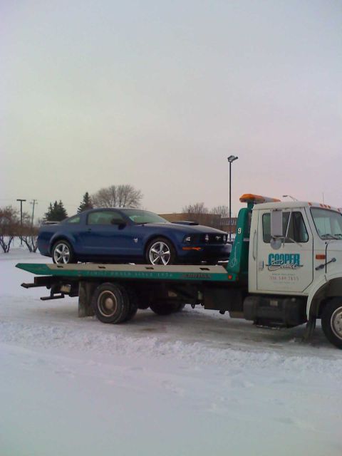 1992 Ford Bronco - A blue Ford Mustang is loaded onto a tow truck in a snowy environment. The tow truck has 'Cooper Auto' branding.