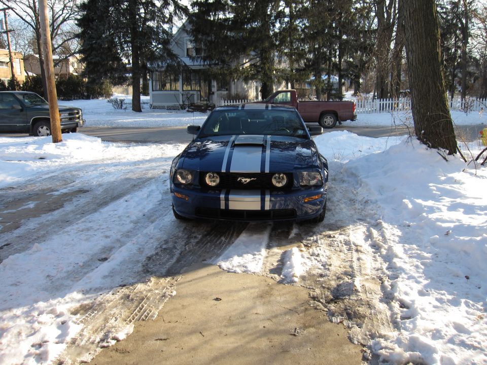 Blue Ford Mustang with silver racing stripes parked in a snowy driveway