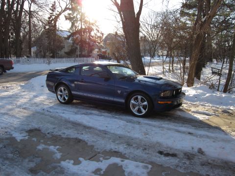 1992 Ford Bronco - A blue Ford Mustang sits on a snow-covered driveway with trees and houses in the background.