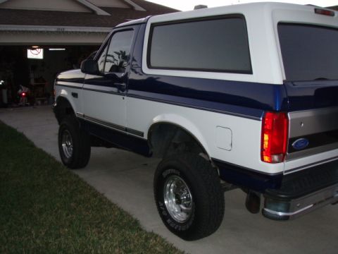 1996 Ford Bronco - A lifted white and blue Ford Bronco is parked in front of a garage.