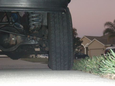 1996 Ford Bronco - Close-up of a vehicle's undercarriage and tire, with houses in the background.