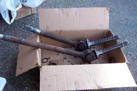 1990 Ford Bronco - Two axle shafts, likely for a 4WD vehicle, sit in a cardboard box. One shaft has a ribbed boot.