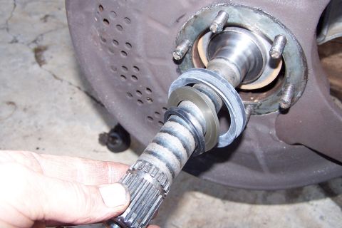 1990 Ford Bronco - Close-up of a splined axle shaft being held, with seals and part of a bearing assembly visible.